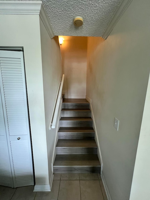 staircase featuring tile patterned flooring, a textured ceiling, and crown molding