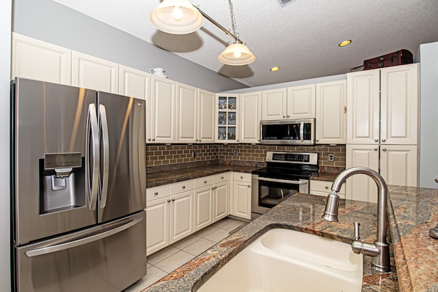 kitchen with a textured ceiling, decorative light fixtures, dark stone countertops, and stainless steel appliances