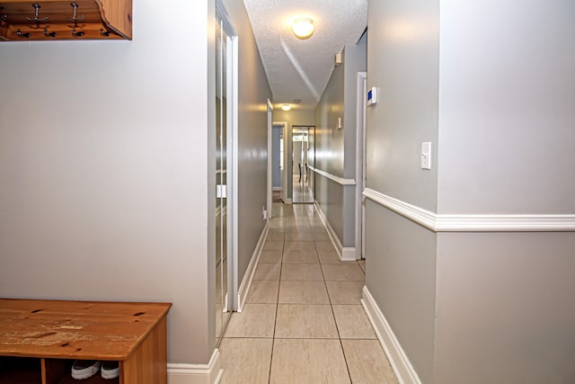 corridor with vaulted ceiling, light tile patterned floors, and a textured ceiling