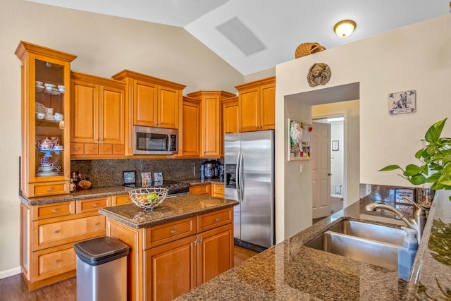 kitchen with sink, vaulted ceiling, decorative backsplash, dark stone countertops, and stainless steel appliances