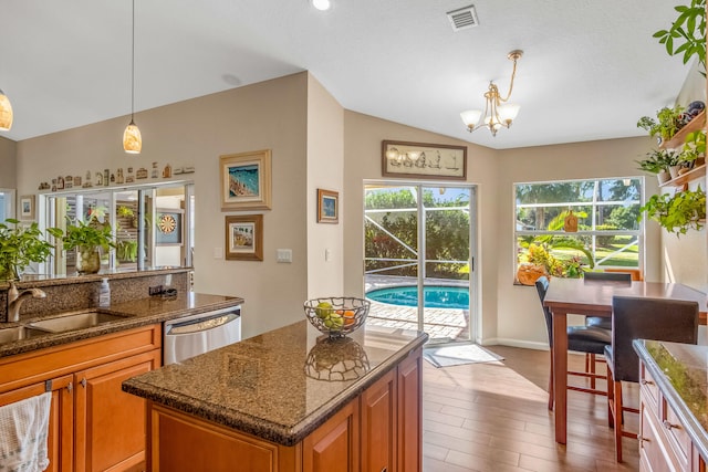 kitchen with dishwasher, dark stone counters, sink, decorative light fixtures, and wood-type flooring