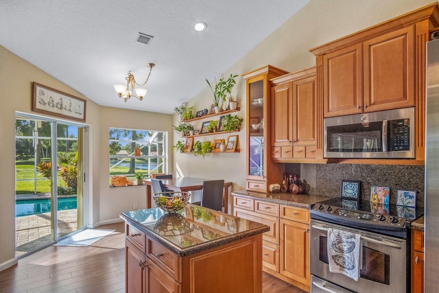 kitchen with appliances with stainless steel finishes, tasteful backsplash, vaulted ceiling, wood-type flooring, and a kitchen island