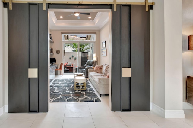 entrance foyer with a tray ceiling, a barn door, ceiling fan, and light tile patterned flooring