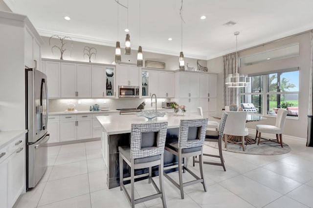 kitchen featuring ornamental molding, a center island with sink, pendant lighting, and appliances with stainless steel finishes