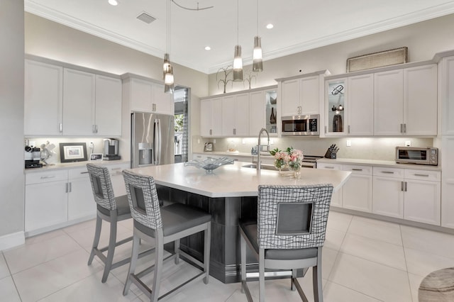 kitchen with appliances with stainless steel finishes, ornamental molding, decorative light fixtures, white cabinetry, and an island with sink