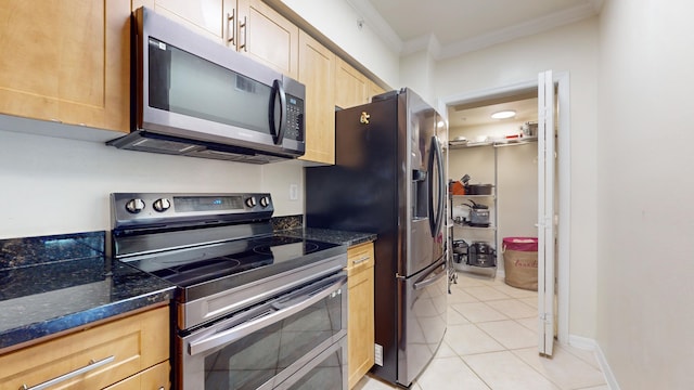 kitchen featuring appliances with stainless steel finishes, light brown cabinetry, ornamental molding, light tile patterned floors, and dark stone countertops