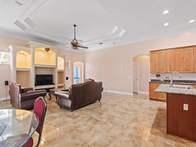 living room with a tray ceiling, ceiling fan, ornamental molding, and sink