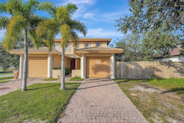 mediterranean / spanish-style home featuring stucco siding, an attached garage, decorative driveway, and fence