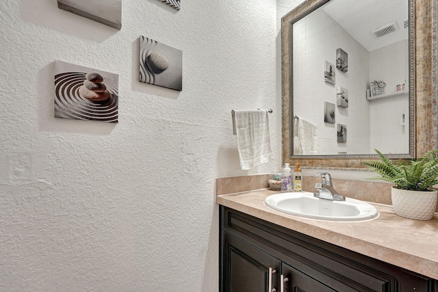 bathroom with vanity, a textured wall, and visible vents