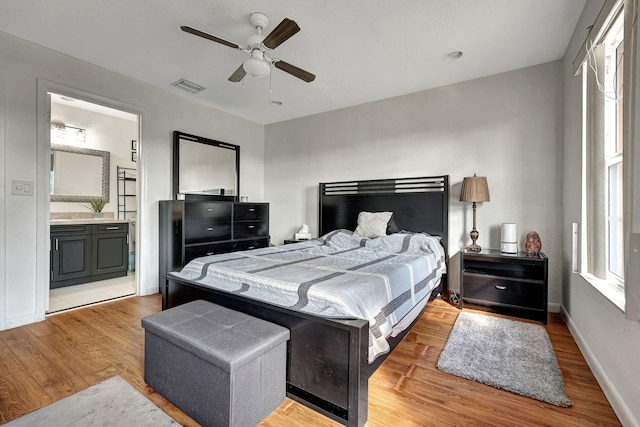 bedroom with visible vents, baseboards, ceiling fan, light wood-style flooring, and ensuite bath