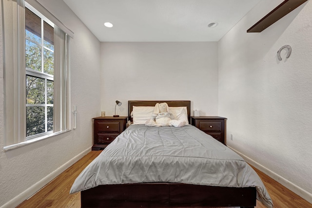 bedroom with recessed lighting, baseboards, wood finished floors, and a textured wall