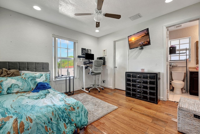 bedroom with ensuite bath, visible vents, a textured ceiling, and wood finished floors