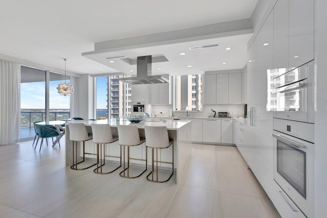 kitchen with a large island, floor to ceiling windows, white cabinets, island exhaust hood, and oven