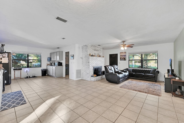 tiled living room with ceiling fan, a fireplace, and a wealth of natural light