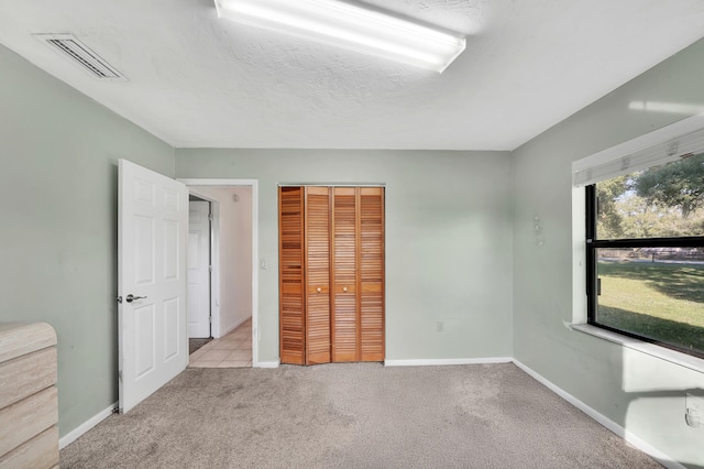 unfurnished bedroom with a closet, light colored carpet, and a textured ceiling