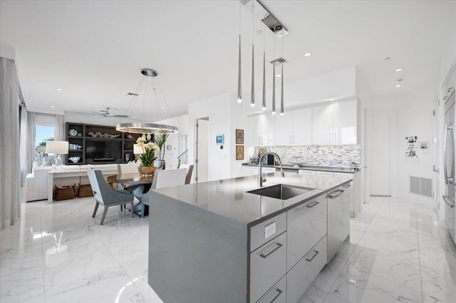 kitchen with backsplash, decorative light fixtures, sink, and a kitchen island with sink