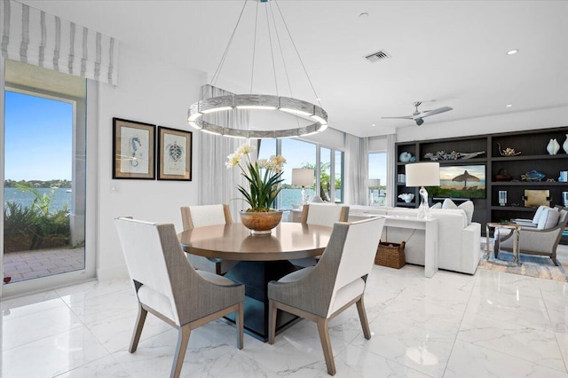 dining space featuring ceiling fan with notable chandelier, a healthy amount of sunlight, and a water view