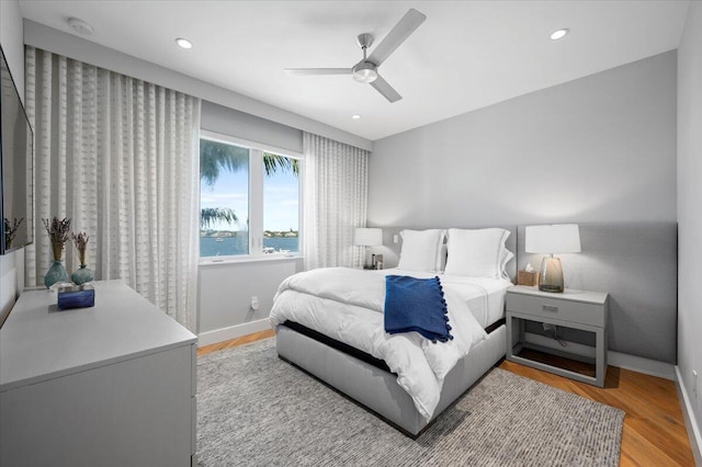 bedroom featuring ceiling fan, a water view, and light wood-type flooring