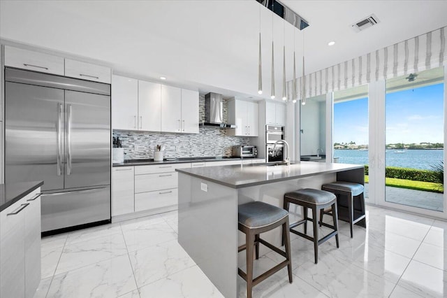 kitchen featuring a breakfast bar, pendant lighting, a water view, stainless steel built in fridge, and an island with sink