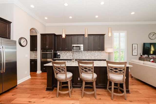 kitchen with hanging light fixtures, light hardwood / wood-style floors, a kitchen bar, a center island with sink, and appliances with stainless steel finishes