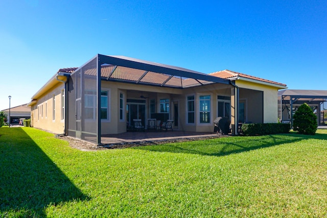 rear view of house with a lawn, glass enclosure, ceiling fan, and a patio