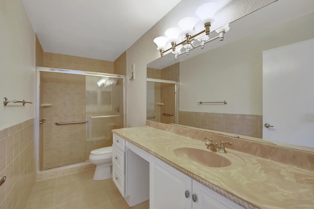 bathroom featuring vanity, toilet, tile walls, and a shower with shower door