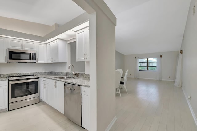 kitchen featuring light stone countertops, stainless steel appliances, sink, light hardwood / wood-style flooring, and white cabinetry