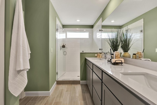 full bathroom with double vanity, a stall shower, a sink, and baseboards