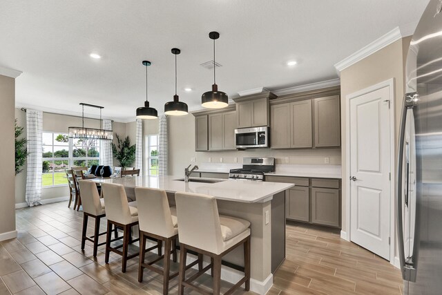 kitchen featuring a kitchen island with sink, gray cabinetry, stainless steel appliances, a sink, and crown molding