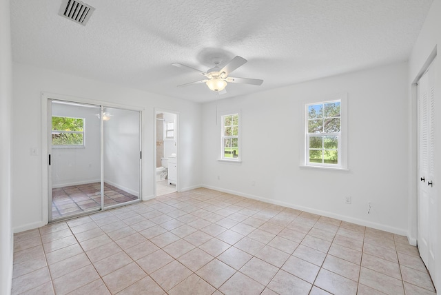 unfurnished bedroom with ceiling fan, light tile patterned flooring, a textured ceiling, and multiple windows