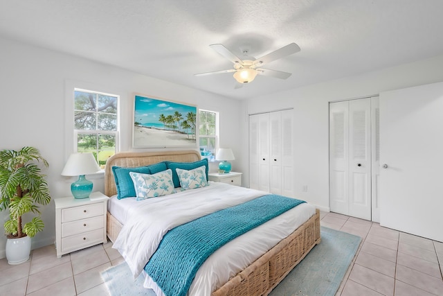 tiled bedroom with ceiling fan, a textured ceiling, and multiple closets