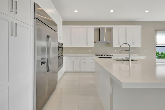 kitchen with appliances with stainless steel finishes, sink, wall chimney range hood, white cabinetry, and light tile patterned flooring