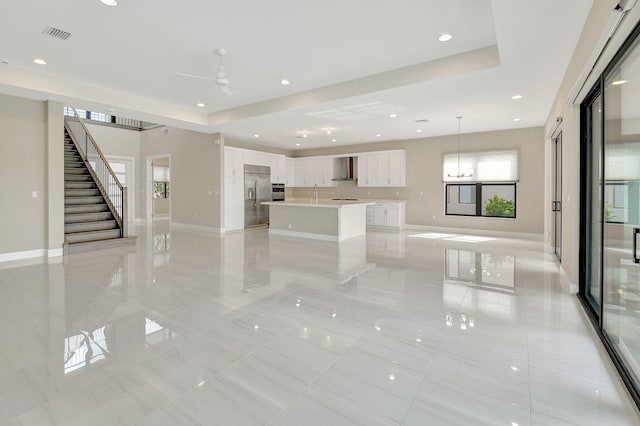 unfurnished living room with a raised ceiling, ceiling fan, and sink