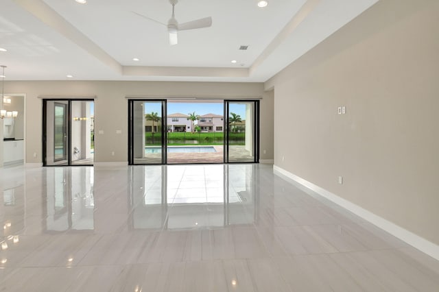 spare room featuring a tray ceiling and ceiling fan with notable chandelier