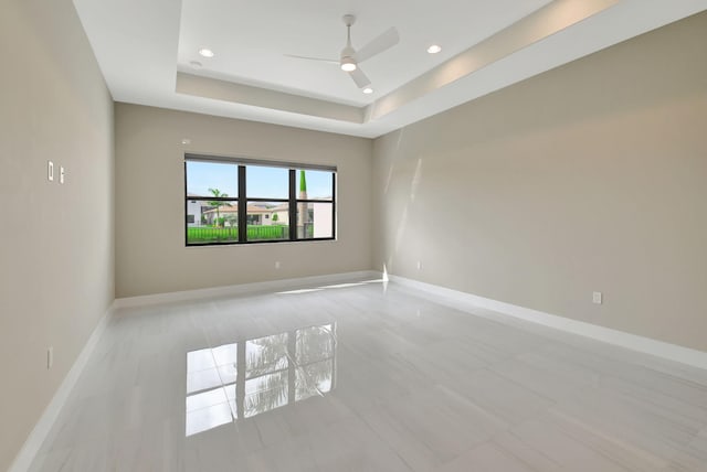 empty room with ceiling fan and a raised ceiling