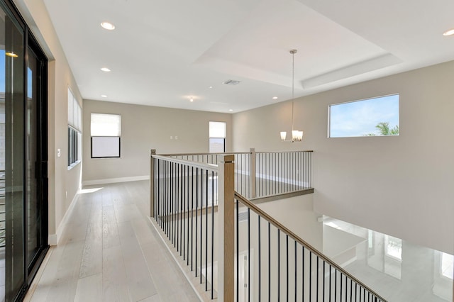 hall featuring a chandelier, light hardwood / wood-style floors, a tray ceiling, and a healthy amount of sunlight