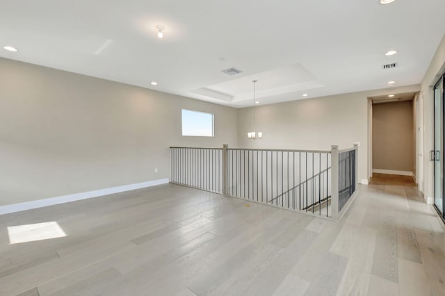 unfurnished room featuring a chandelier, light wood-type flooring, and a raised ceiling