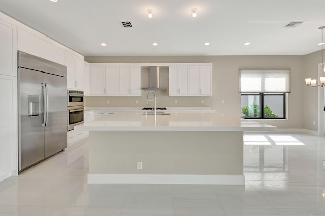 kitchen featuring white cabinets, an island with sink, wall chimney exhaust hood, and stainless steel appliances