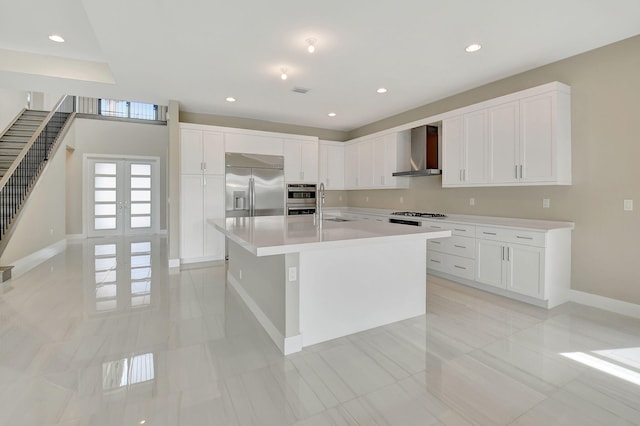 kitchen featuring french doors, wall chimney range hood, an island with sink, white cabinetry, and stainless steel appliances