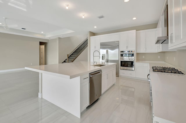 kitchen featuring a kitchen island with sink, white cabinets, a raised ceiling, sink, and appliances with stainless steel finishes