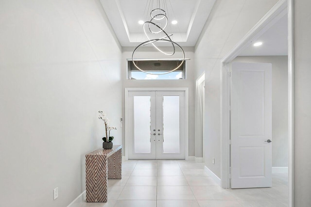 foyer with french doors, light tile patterned floors, an inviting chandelier, and a raised ceiling