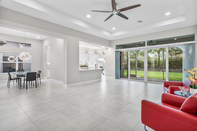 living room featuring a raised ceiling, ceiling fan, and light tile patterned floors