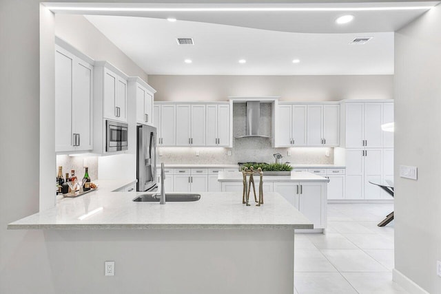 kitchen with white cabinetry, sink, wall chimney exhaust hood, stainless steel appliances, and kitchen peninsula