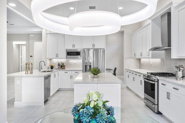 kitchen featuring wall chimney exhaust hood, sink, built in appliances, decorative light fixtures, and a center island with sink