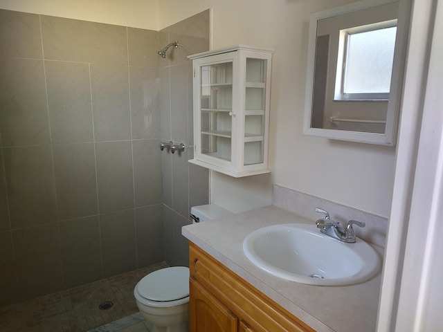 bathroom with toilet, a tile shower, and vanity