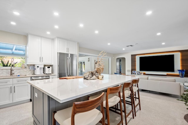 kitchen with a breakfast bar, stainless steel appliances, a kitchen island, sink, and white cabinetry