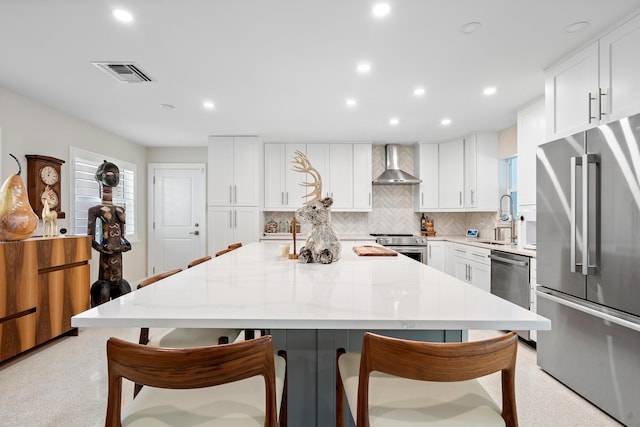 kitchen with light stone counters, stainless steel appliances, sink, wall chimney range hood, and white cabinets