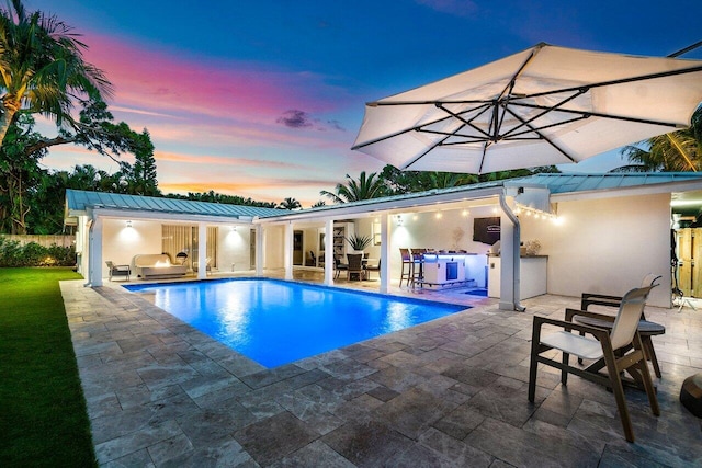 pool at dusk with exterior kitchen and a patio