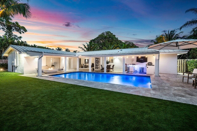 back house at dusk featuring exterior kitchen, a yard, and a patio