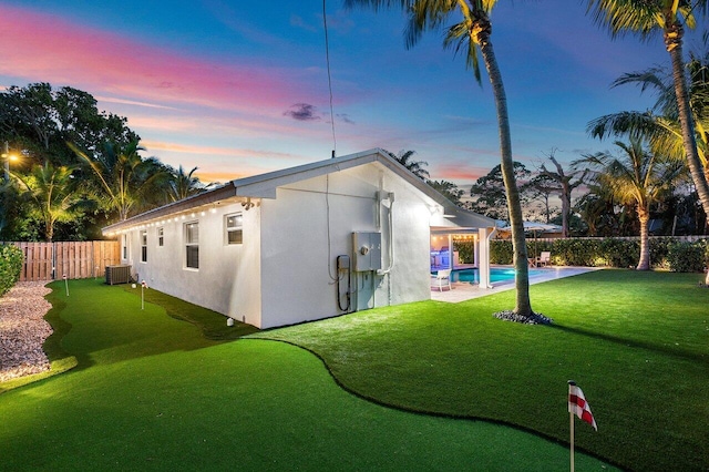 back house at dusk featuring a fenced in pool and central AC